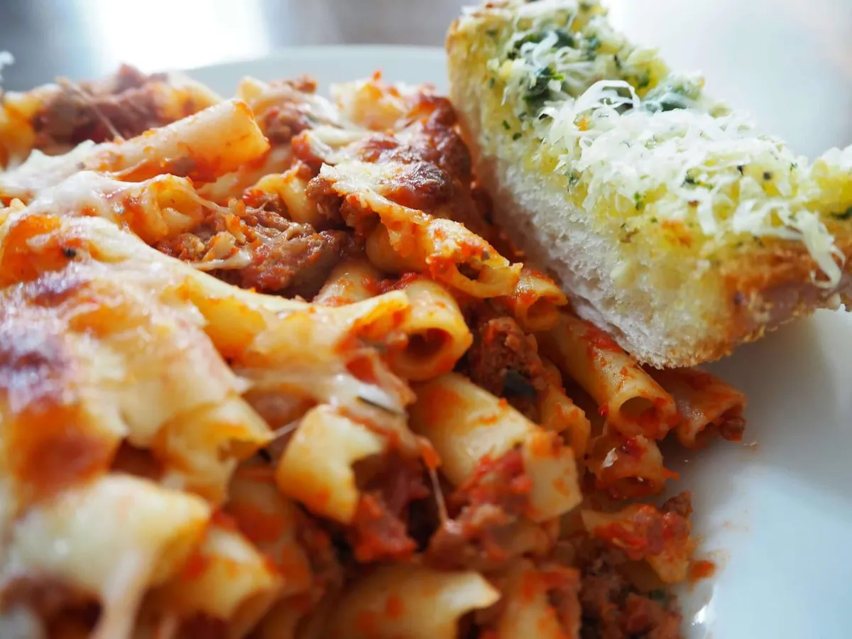Baked ziti with melted cheese beside a slice of garlic bread