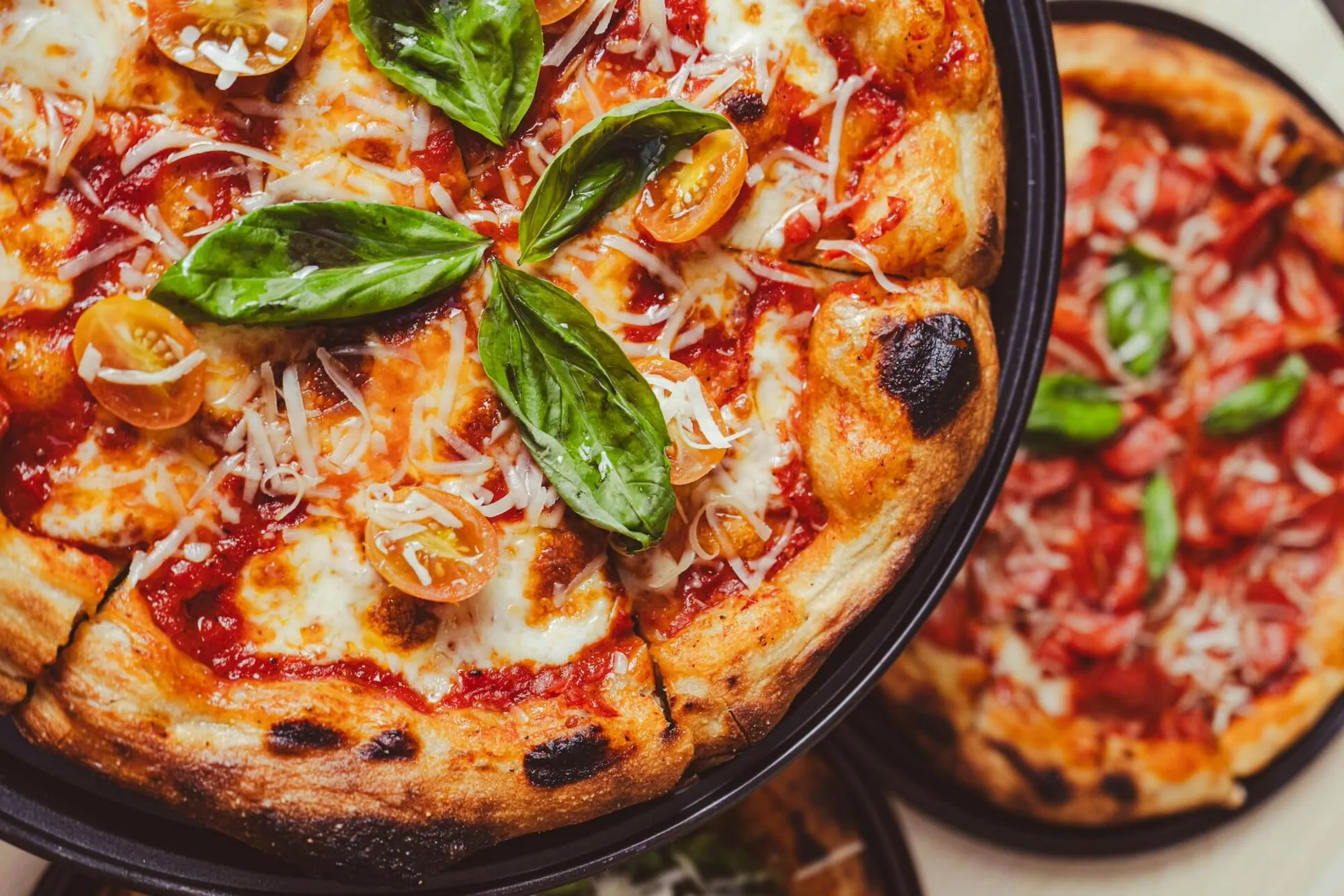 Pizza with a charred crust, basil leaves, halved cherry tomatoes and melted cheese